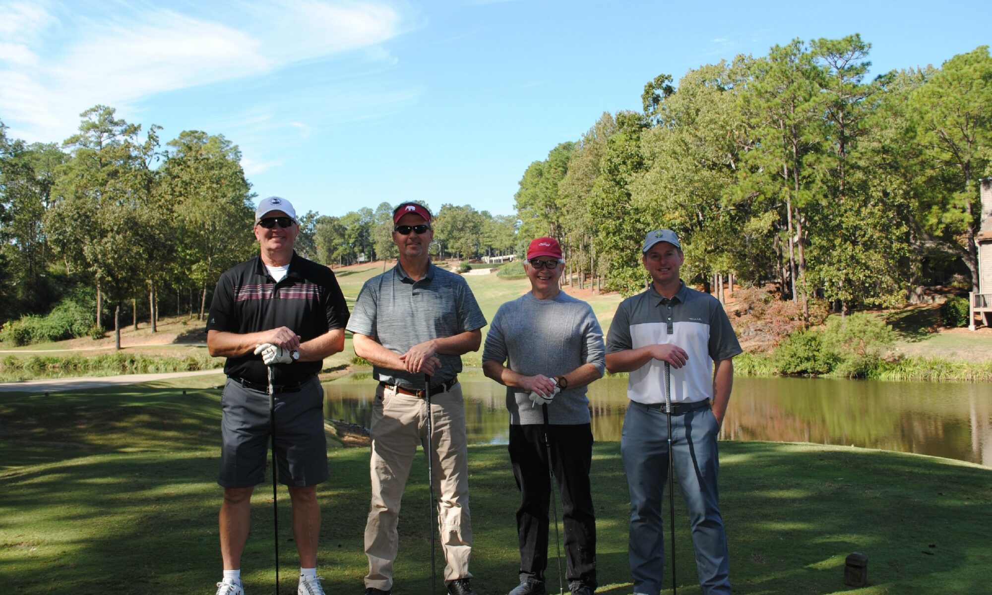 Four men standing with golf clubs on a sunny golf course.