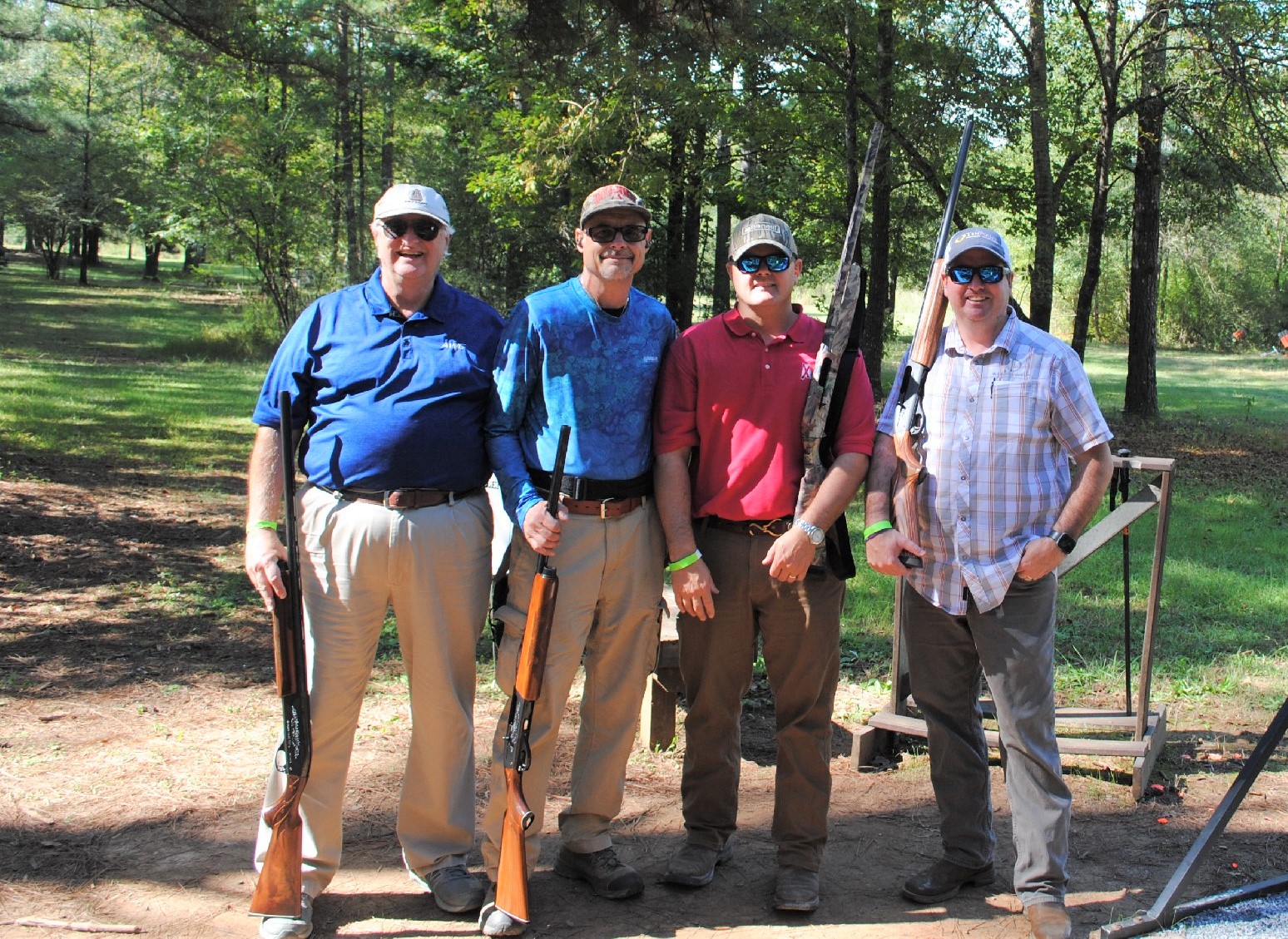 Four men outdoors holding rifles, dressed in casual shooting attire.