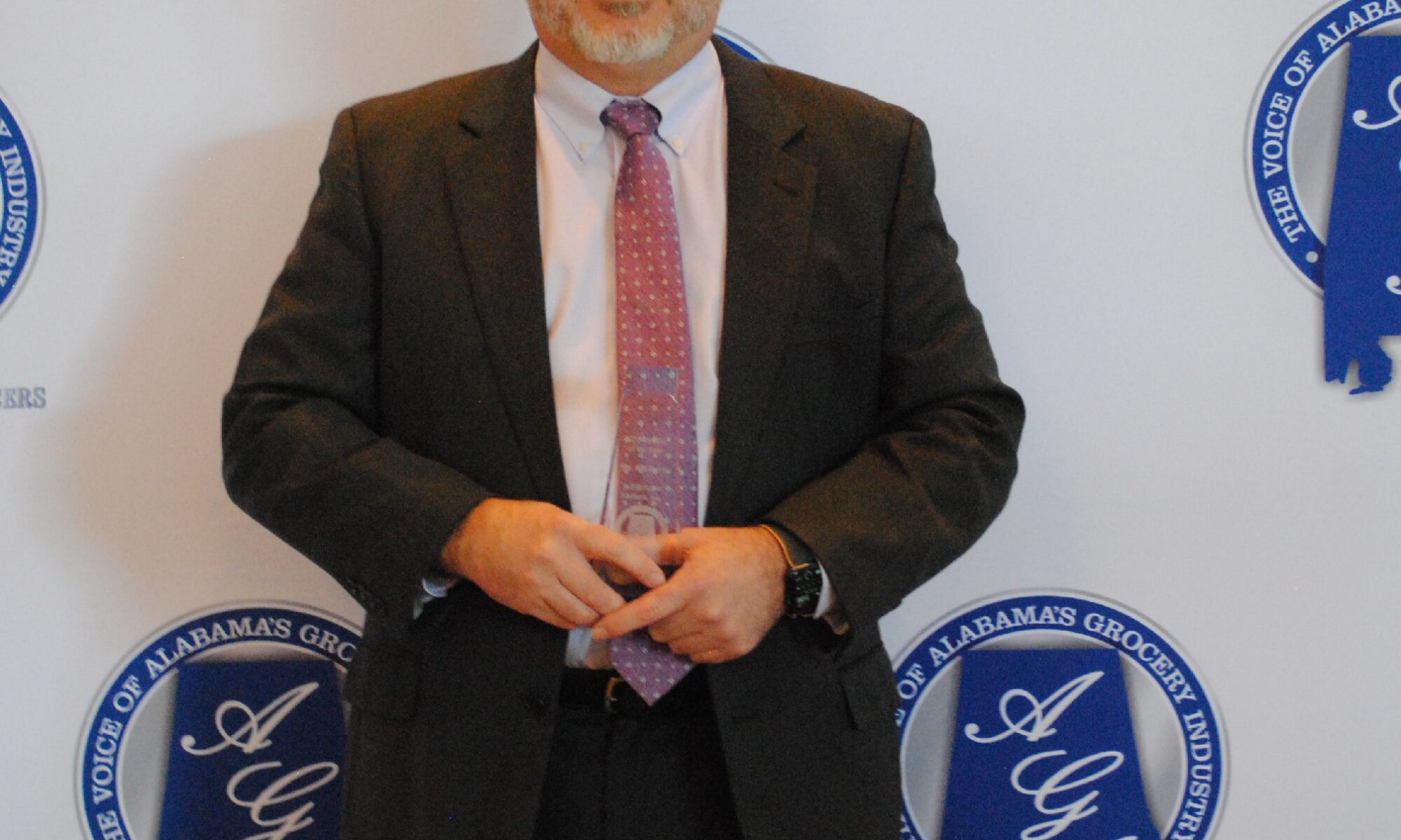Man in suit standing in front of a branded backdrop.