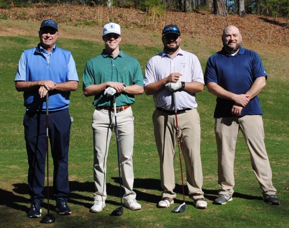 Four men in golf attire standing on a golf course holding clubs.