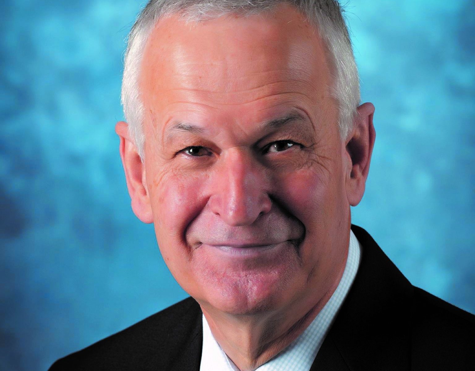Portrait of a smiling elderly man in a suit with a green tie.
