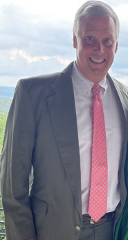 Man in a suit with a red tie smiling outdoors.