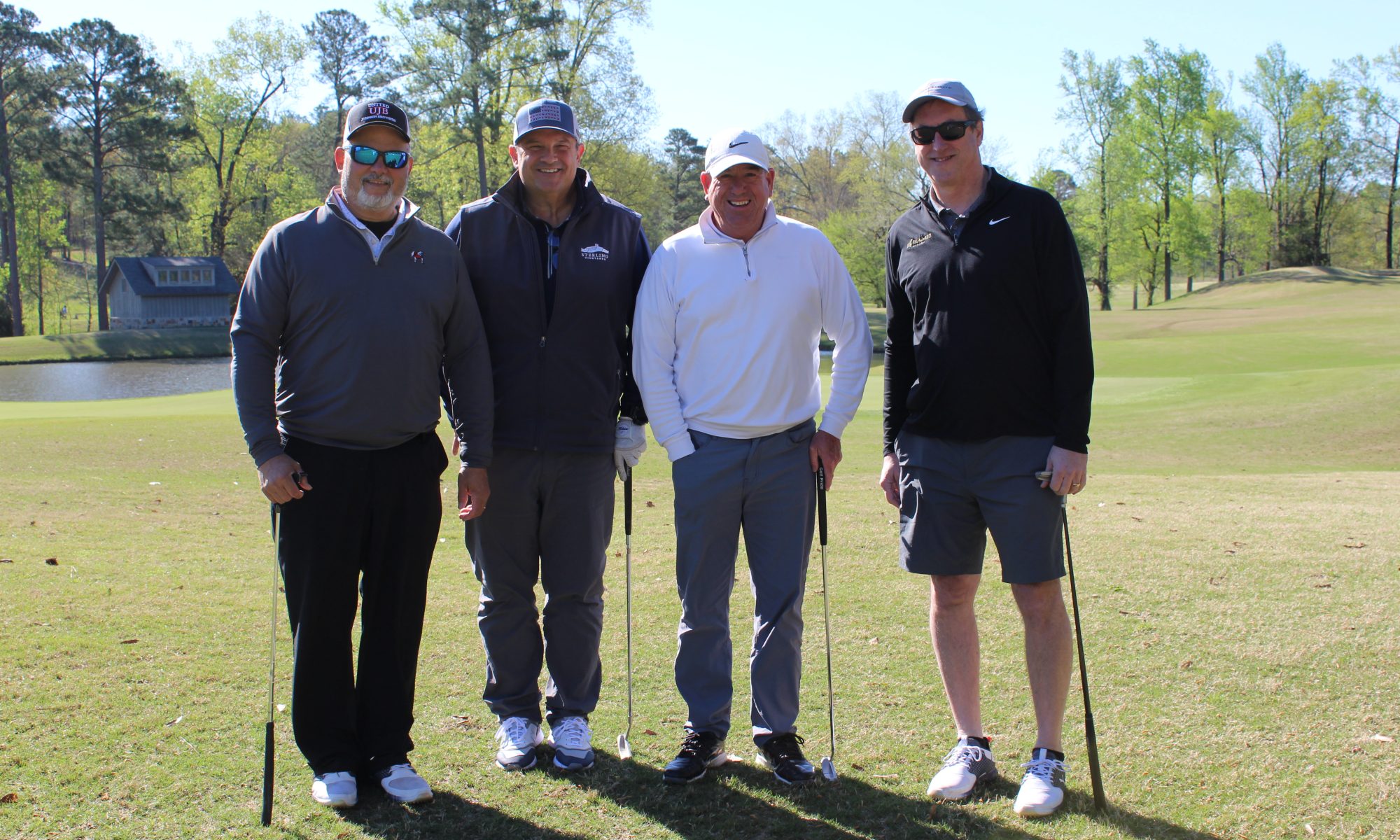 Four men posing with golf clubs on a sunny golf course.